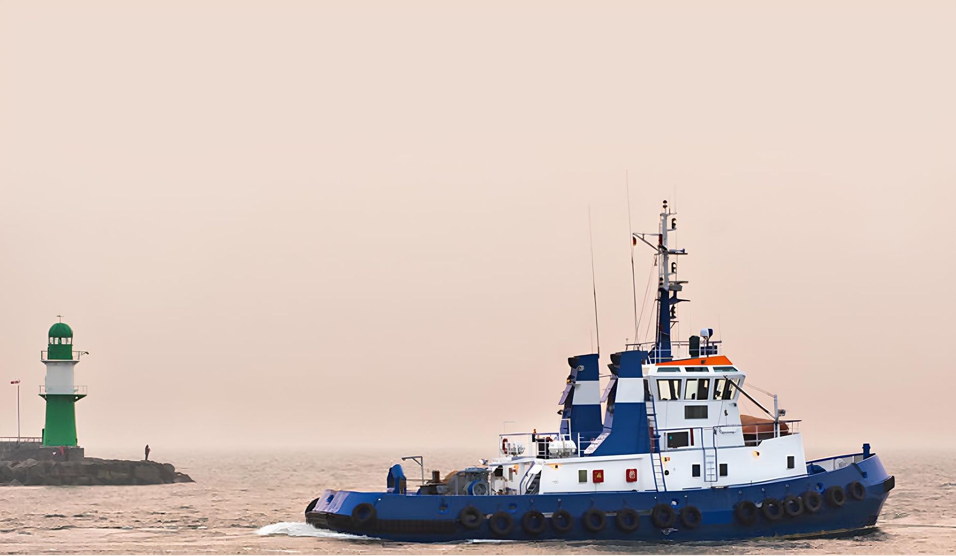 Ein blau-weißer Schlepper fährt auf ruhigem Wasser in der Nähe eines grünen Leuchtturms